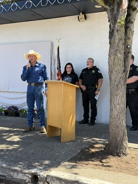 A speaker addresses the crowd at the Chief Woody Whetstone memorial dedication while Junction City police officers stand behind the podium.